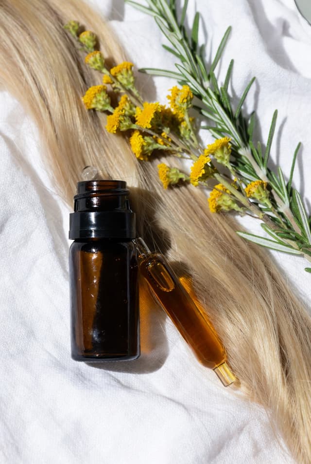 Flesje haarserum op lang blond haar met gele bloemen en rozemarijn